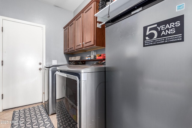 clothes washing area with cabinets, washer and dryer, and light tile patterned floors