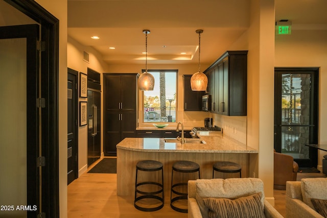 kitchen with a peninsula, a sink, a kitchen breakfast bar, light stone countertops, and decorative light fixtures