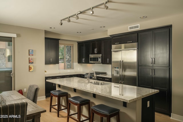 kitchen with visible vents, appliances with stainless steel finishes, a kitchen island with sink, and light stone countertops