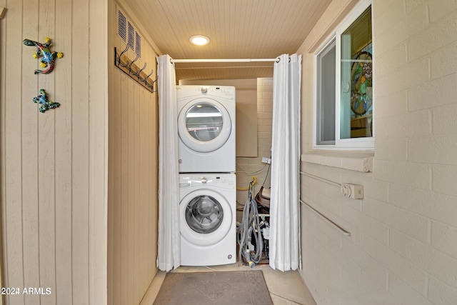 clothes washing area featuring stacked washer / dryer, wooden walls, and brick wall