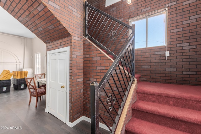 stairs with brick wall, dark hardwood / wood-style flooring, and vaulted ceiling