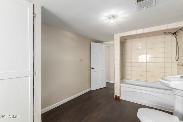 bathroom featuring wood-type flooring, tiled shower / bath combo, and toilet