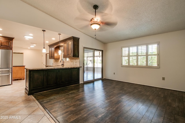 kitchen featuring tasteful backsplash, a sink, ceiling fan, light stone countertops, and stainless steel fridge