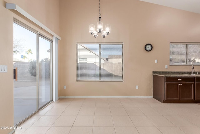 unfurnished dining area featuring a notable chandelier, a towering ceiling, sink, and light tile patterned floors