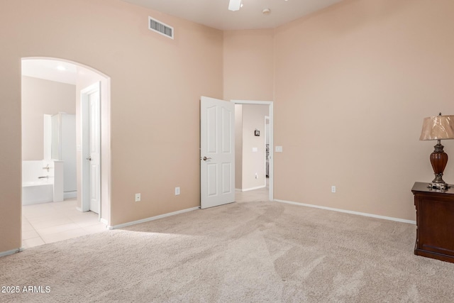 unfurnished bedroom with ceiling fan, ensuite bath, and light colored carpet