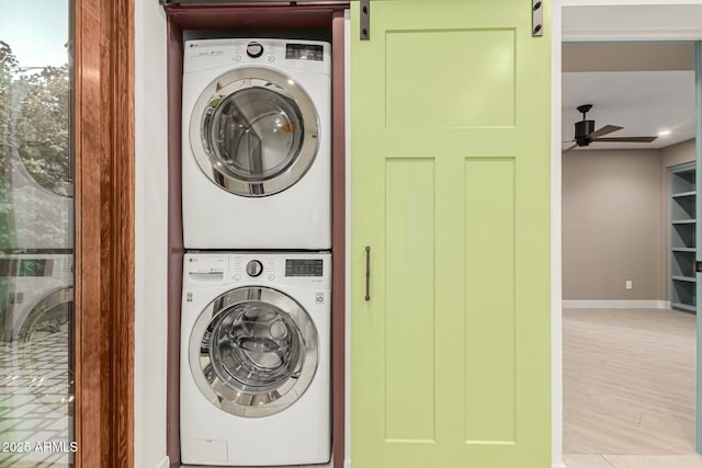 laundry area featuring ceiling fan, a barn door, light hardwood / wood-style floors, and stacked washer / dryer