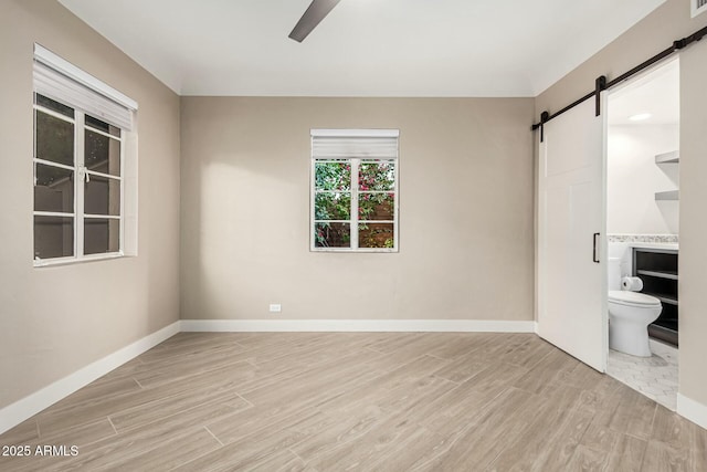 unfurnished bedroom with a barn door, ensuite bath, and ceiling fan