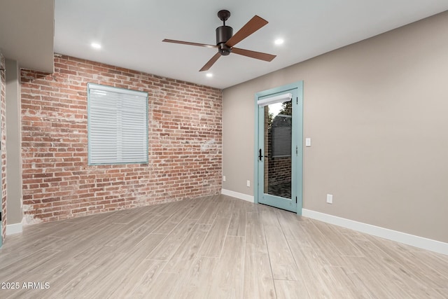 spare room featuring ceiling fan, brick wall, and light hardwood / wood-style flooring