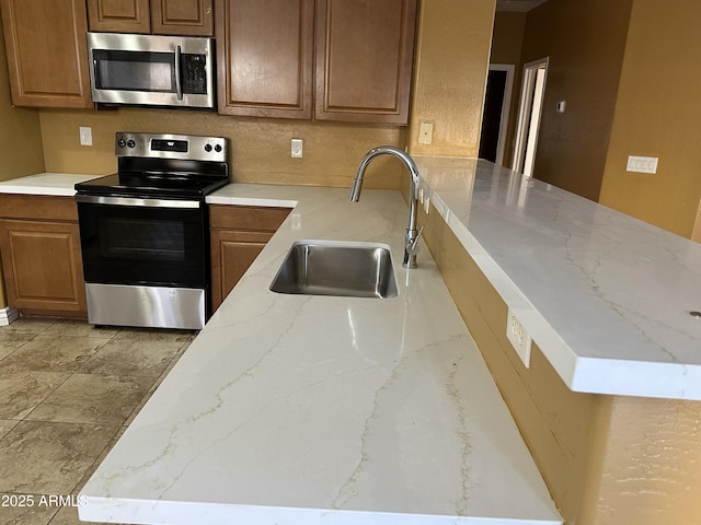 7511 S 45th Dr, Laveen, AZ 85339 - kitchen with brown cabinets, a sink, light stone counters, stainless steel appliances, and a peninsula