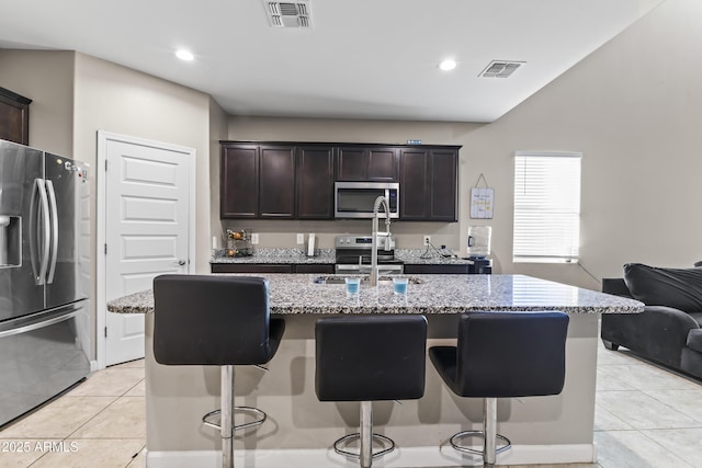 kitchen featuring appliances with stainless steel finishes, a kitchen island with sink, visible vents, and dark brown cabinetry