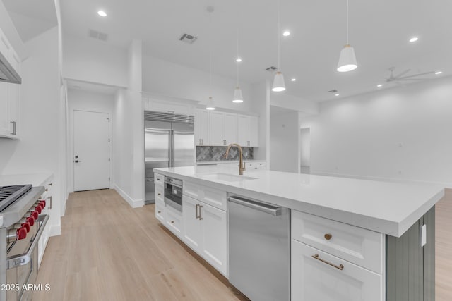 kitchen featuring decorative light fixtures, white cabinetry, sink, high end appliances, and a kitchen island with sink