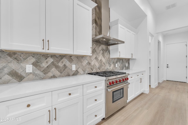 kitchen featuring tasteful backsplash, wall chimney exhaust hood, premium range, and white cabinets