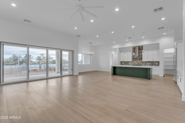 unfurnished living room featuring ceiling fan with notable chandelier and light wood-type flooring