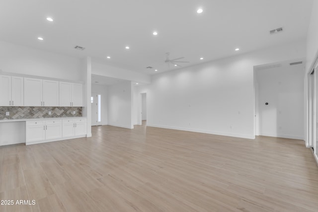 unfurnished living room with light hardwood / wood-style flooring, built in desk, and ceiling fan