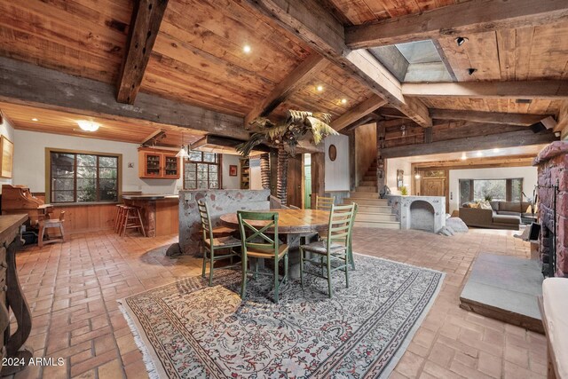 dining space with wooden walls, vaulted ceiling with skylight, and wood ceiling