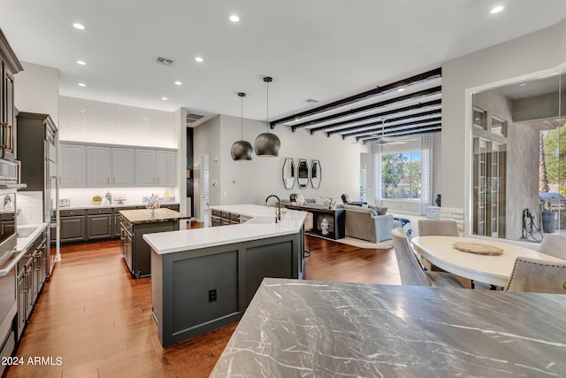 kitchen with pendant lighting, backsplash, a kitchen island with sink, dark wood-type flooring, and gray cabinets