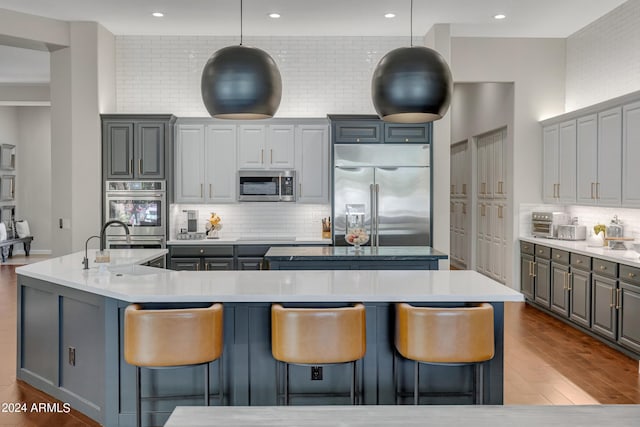 kitchen with tasteful backsplash, gray cabinetry, an island with sink, and stainless steel appliances