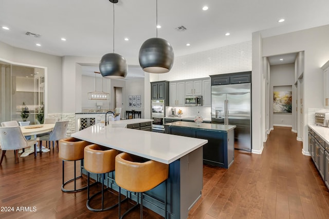 kitchen with hanging light fixtures, stainless steel appliances, a kitchen island with sink, and a breakfast bar area