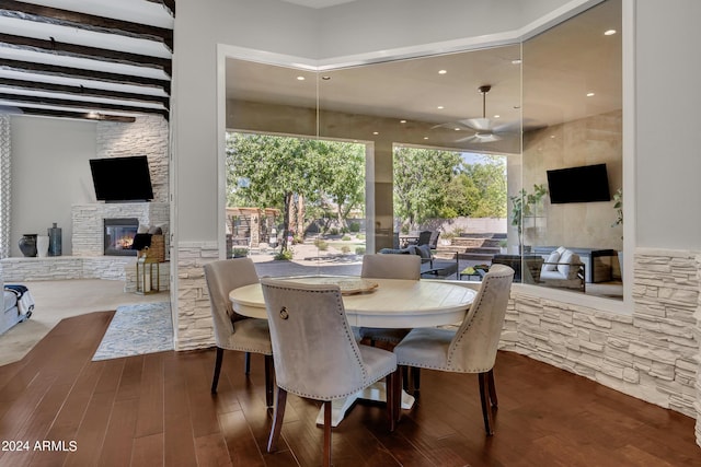 dining space with beam ceiling, a stone fireplace, ceiling fan, and dark hardwood / wood-style flooring