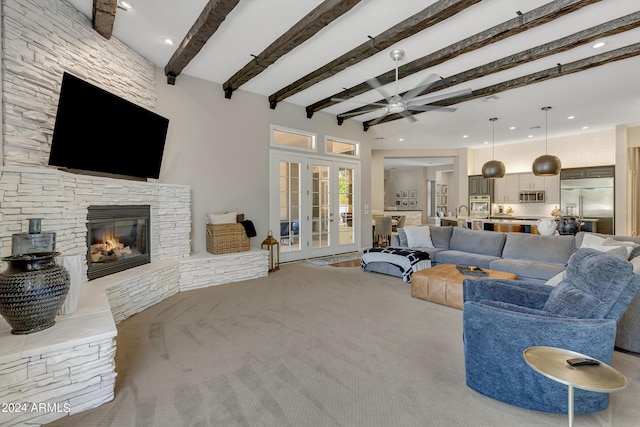 living room featuring french doors, a stone fireplace, ceiling fan, beamed ceiling, and carpet floors