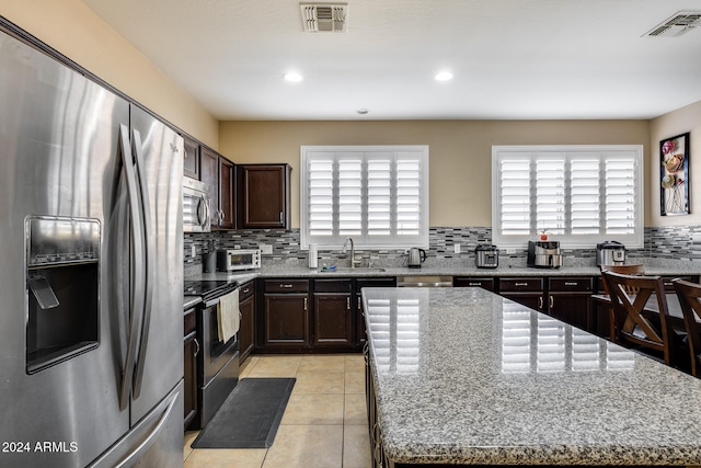 kitchen with appliances with stainless steel finishes, sink, a kitchen island, and light stone counters