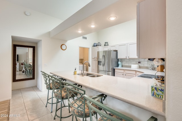 kitchen featuring sink, stainless steel refrigerator with ice dispenser, kitchen peninsula, decorative backsplash, and light tile patterned floors