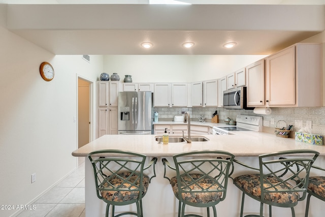 kitchen featuring sink, kitchen peninsula, a kitchen bar, light tile patterned floors, and appliances with stainless steel finishes