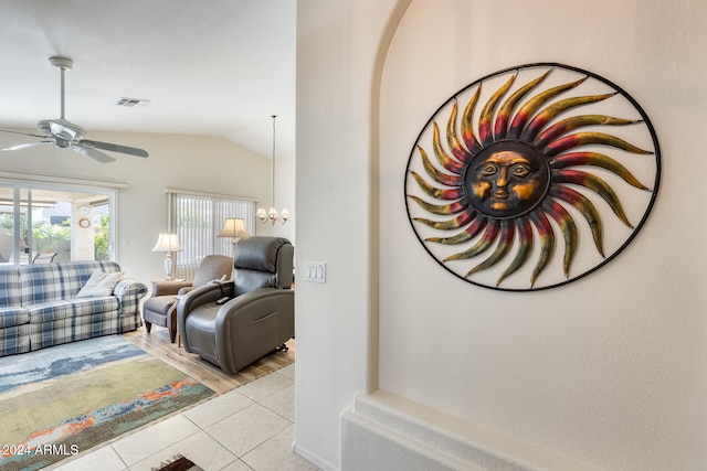 living room with ceiling fan with notable chandelier, light tile patterned floors, and vaulted ceiling