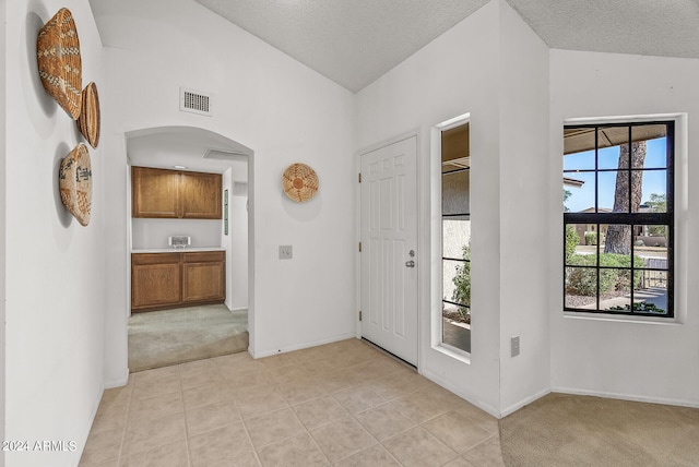 carpeted foyer entrance with a textured ceiling and vaulted ceiling