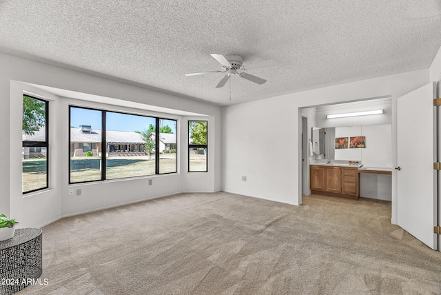 unfurnished living room featuring a textured ceiling, ceiling fan, a healthy amount of sunlight, and light carpet