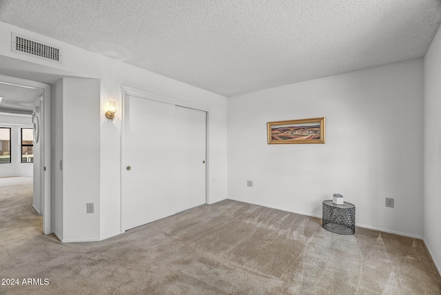 unfurnished bedroom featuring a textured ceiling, light carpet, and a closet