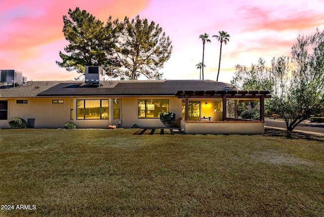 back house at dusk featuring a yard, central AC unit, and solar panels