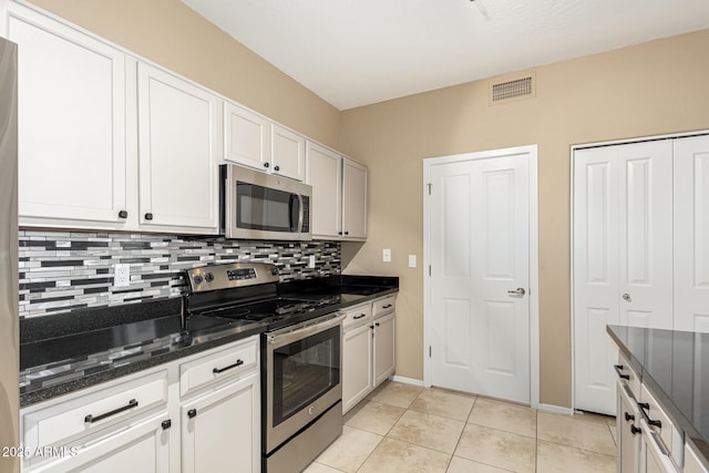 kitchen with white cabinetry, tasteful backsplash, dark stone countertops, light tile patterned floors, and stainless steel appliances