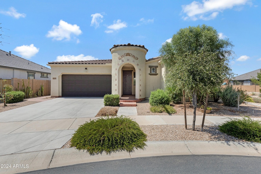 mediterranean / spanish home featuring a tile roof, stucco siding, concrete driveway, fence, and a garage