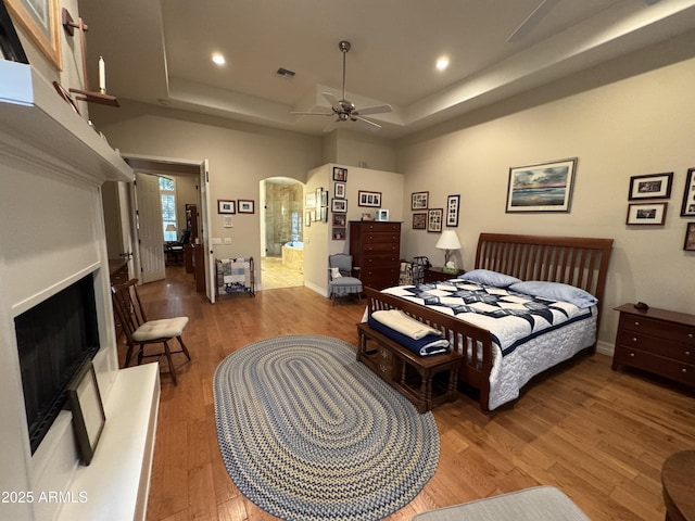 bedroom with hardwood / wood-style flooring, ceiling fan, a tray ceiling, and a towering ceiling