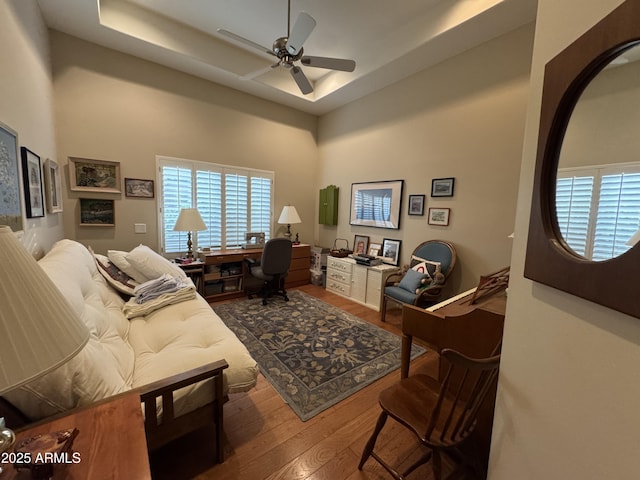 living room with a raised ceiling, hardwood / wood-style floors, and ceiling fan