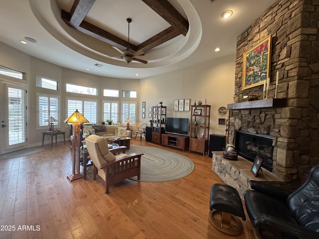 living room featuring ceiling fan, a fireplace, light hardwood / wood-style floors, and a tray ceiling