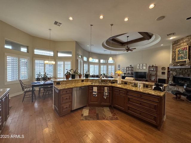 kitchen with a large island, dishwasher, hanging light fixtures, light stone countertops, and a raised ceiling