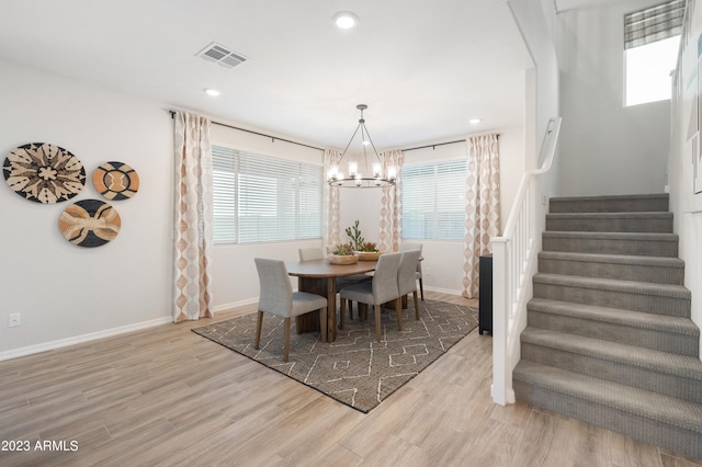 dining area featuring a chandelier, light wood-style flooring, visible vents, baseboards, and stairs