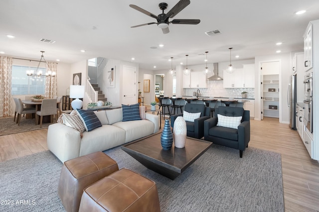 living room with recessed lighting, visible vents, light wood-style flooring, and ceiling fan with notable chandelier