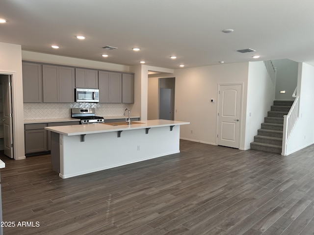 kitchen featuring gray cabinetry, tasteful backsplash, appliances with stainless steel finishes, dark hardwood / wood-style flooring, and an island with sink