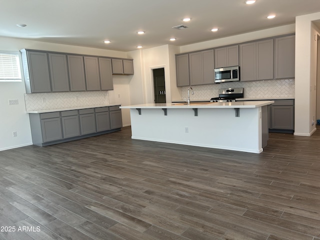 kitchen featuring appliances with stainless steel finishes, an island with sink, and gray cabinetry