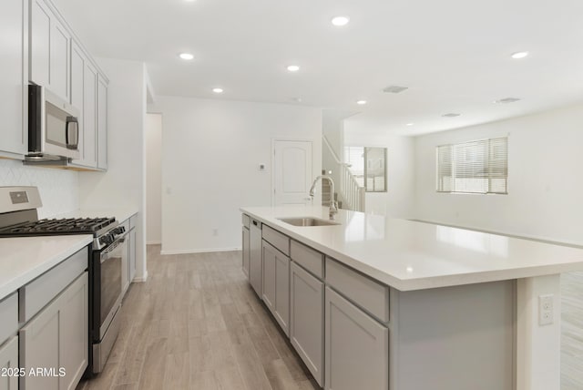 kitchen featuring light countertops, stainless steel appliances, gray cabinetry, light wood-type flooring, and a sink