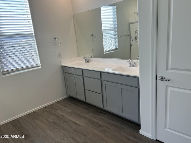 full bath featuring double vanity, a sink, baseboards, and wood finished floors