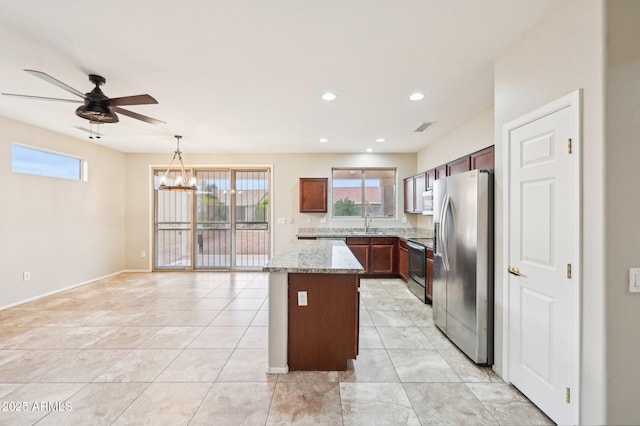 kitchen featuring a center island, light stone counters, ceiling fan with notable chandelier, stainless steel appliances, and a sink