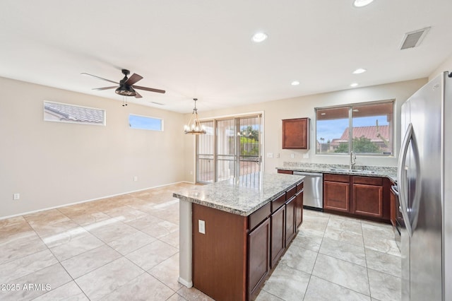 kitchen with light stone countertops, ceiling fan with notable chandelier, appliances with stainless steel finishes, and a sink