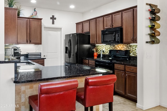 kitchen with a peninsula, black appliances, tasteful backsplash, and a breakfast bar