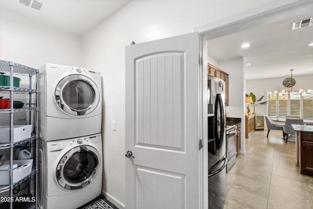 clothes washing area featuring stacked washing maching and dryer, laundry area, visible vents, and light tile patterned flooring