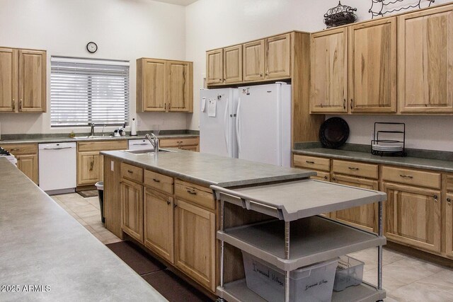 kitchen with white appliances, light brown cabinets, a kitchen island with sink, and a sink