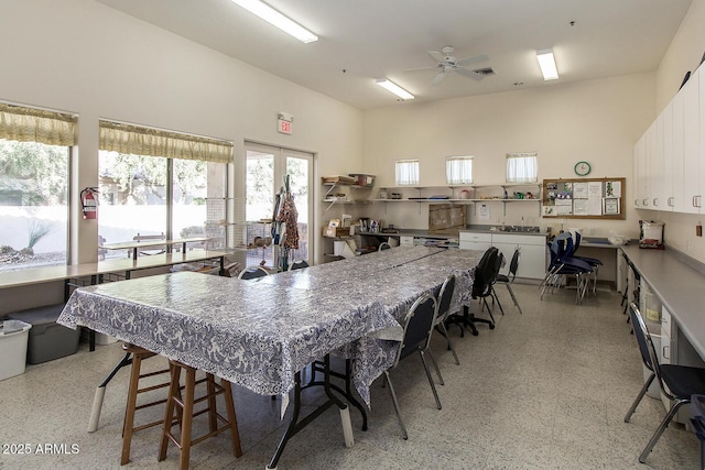 kitchen with light speckled floor, a ceiling fan, a towering ceiling, white cabinetry, and a kitchen breakfast bar